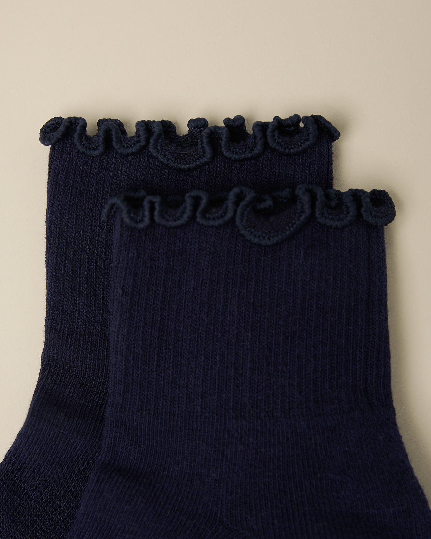 Close up of the ruffle on a pair of Non-Slip Ruffle Ankle Socks in Navy on a beige background.