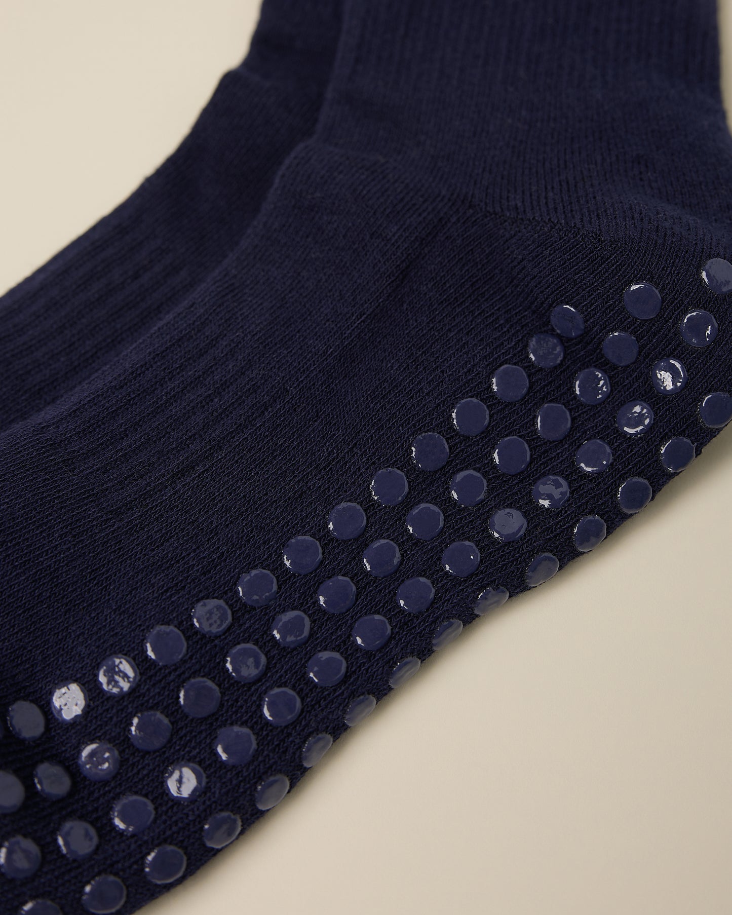 Close up on the non-slip dots on a pair of Non-Slip Ruffle Ankle Socks in Navy on a beige background.