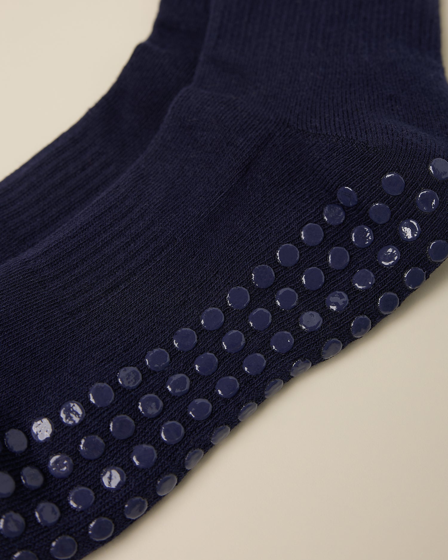 Close up on the non-slip dots on a pair of Non-Slip Ruffle Ankle Socks in Navy on a beige background.