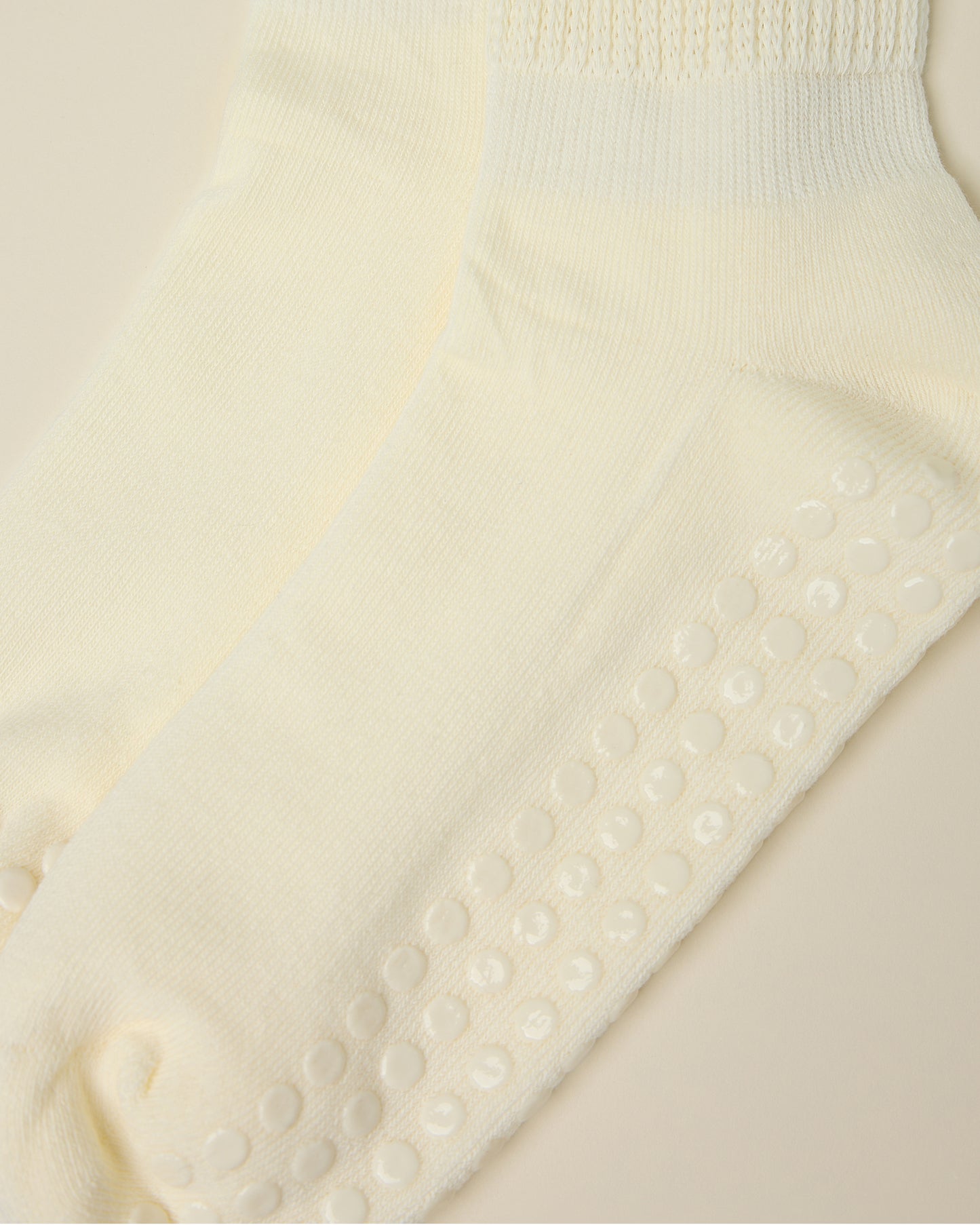 Close up on the non-slip dots on a pair of Non-Slip Slouchy Socks in Cream on a beige background