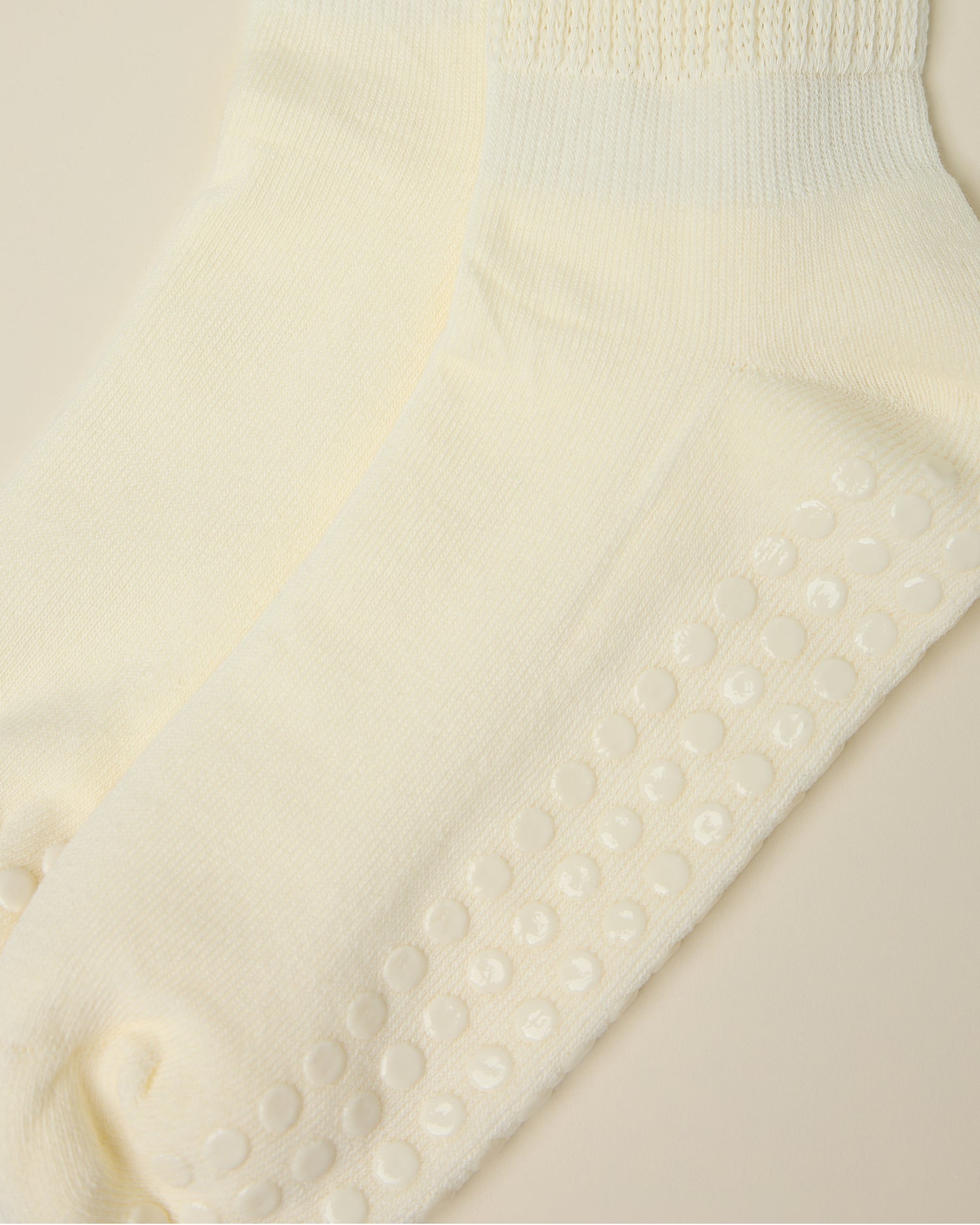 Close up on the non-slip dots on a pair of Non-Slip Slouchy Socks in Cream on a beige background