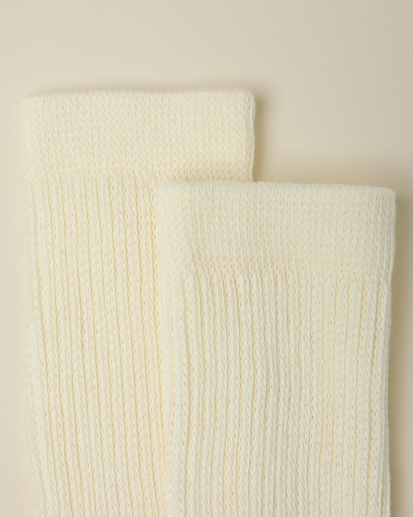 Close up on the cozy cuffs of a pair of Non-Slip Slouchy Socks in Cream on a beige background