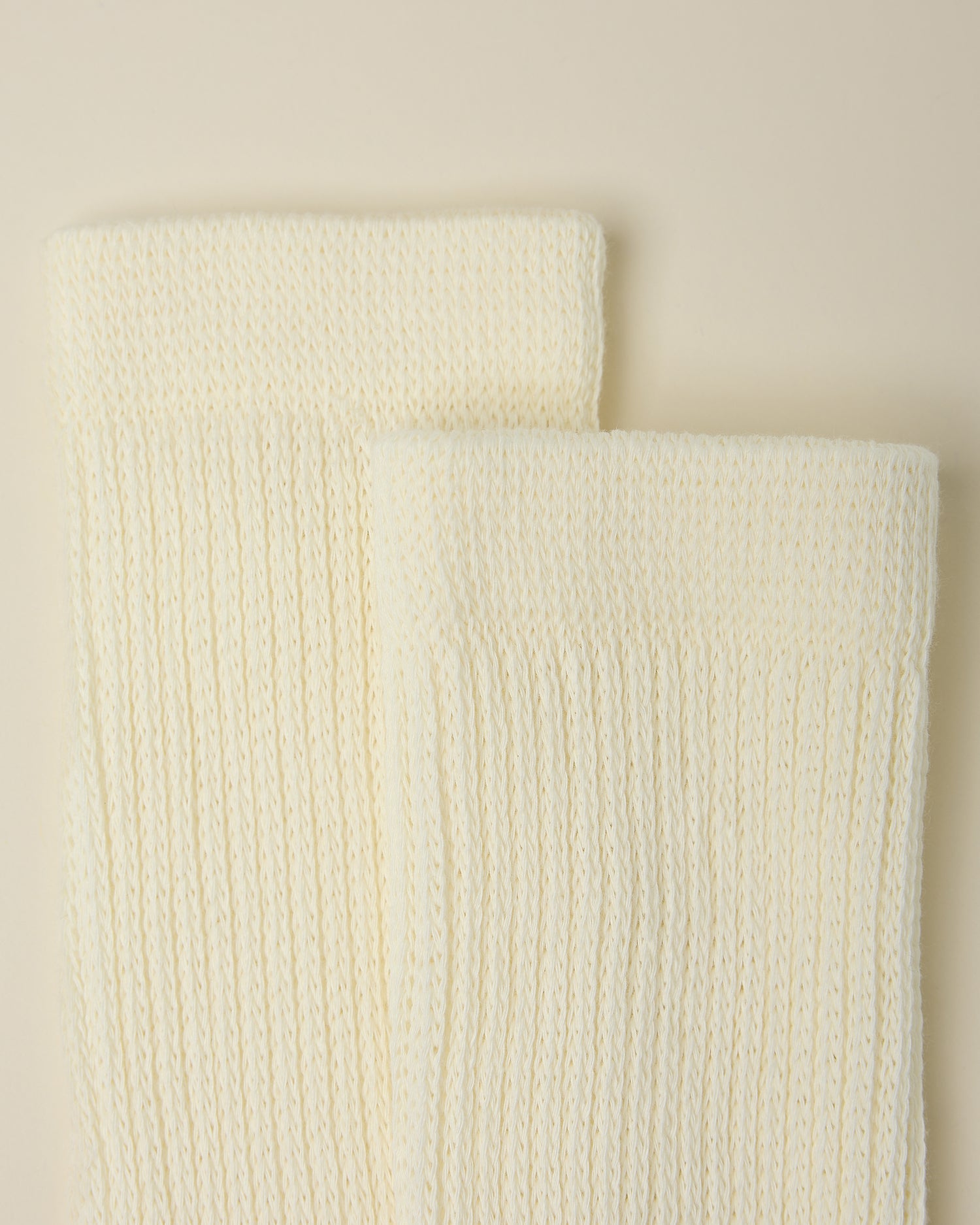 Close up on the cozy cuffs of a pair of Non-Slip Slouchy Socks in Cream on a beige background