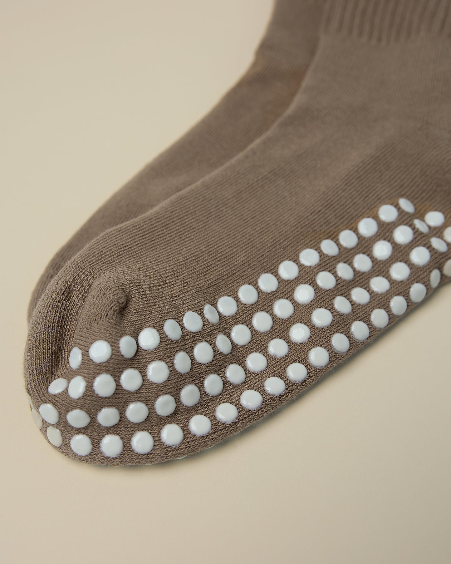 Close up on the white non-slip dots on a pair of Non-Slip Slouchy Socks in Taupe on a beige background