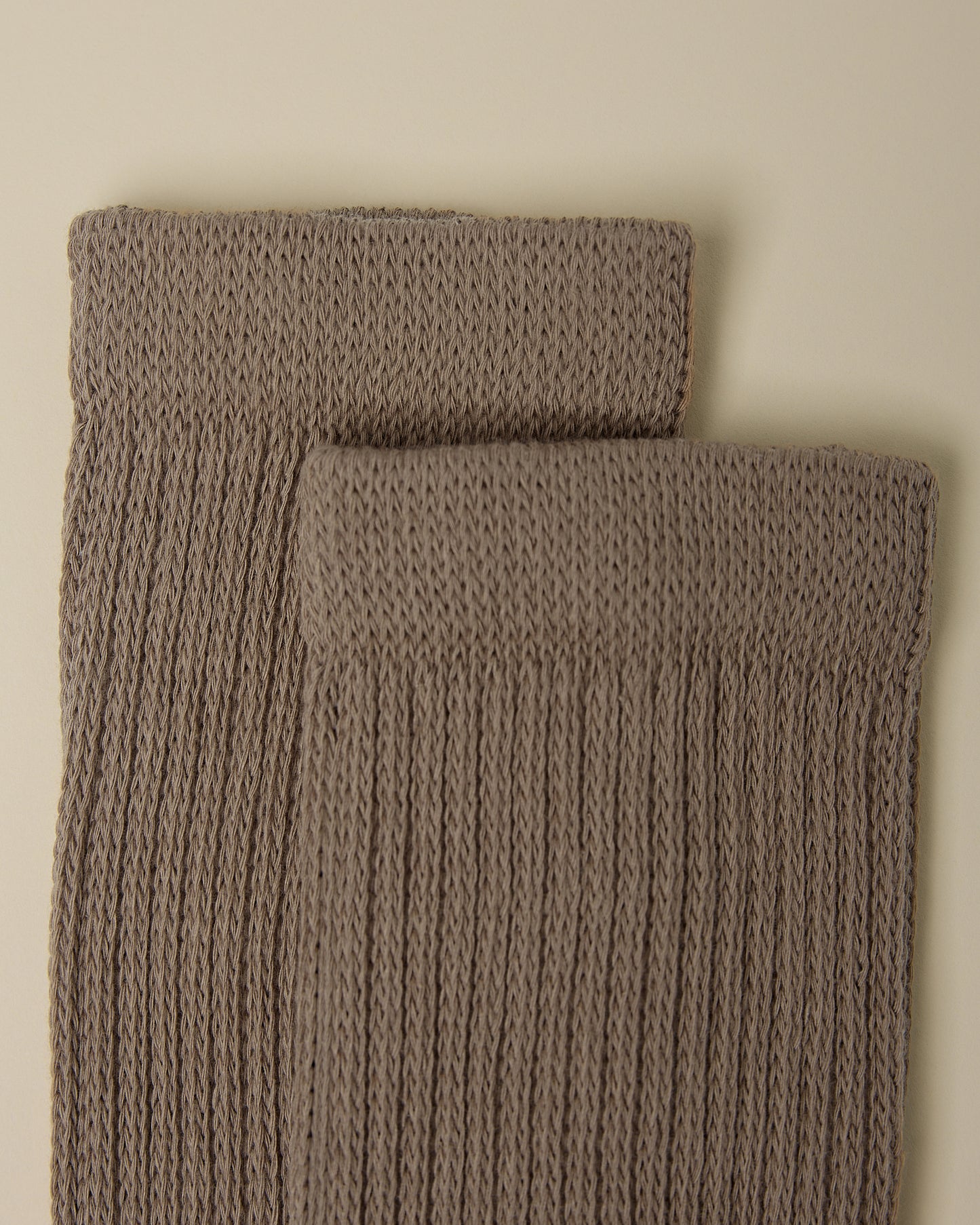Close up on the cozy cuffs of a pair of Non-Slip Slouchy Socks in Taupe on a beige background