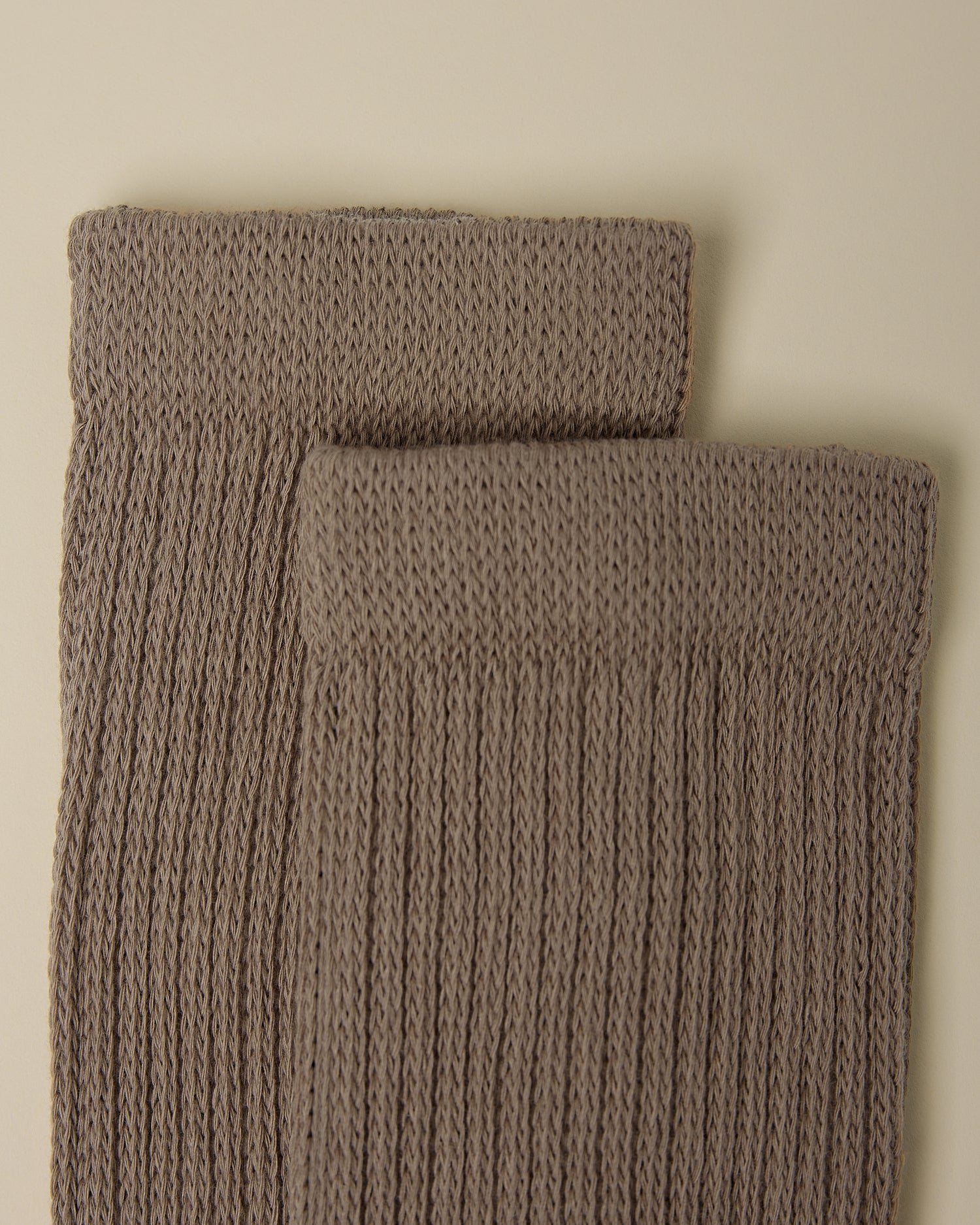 Close up on the cozy cuffs of a pair of Non-Slip Slouchy Socks in Taupe on a beige background