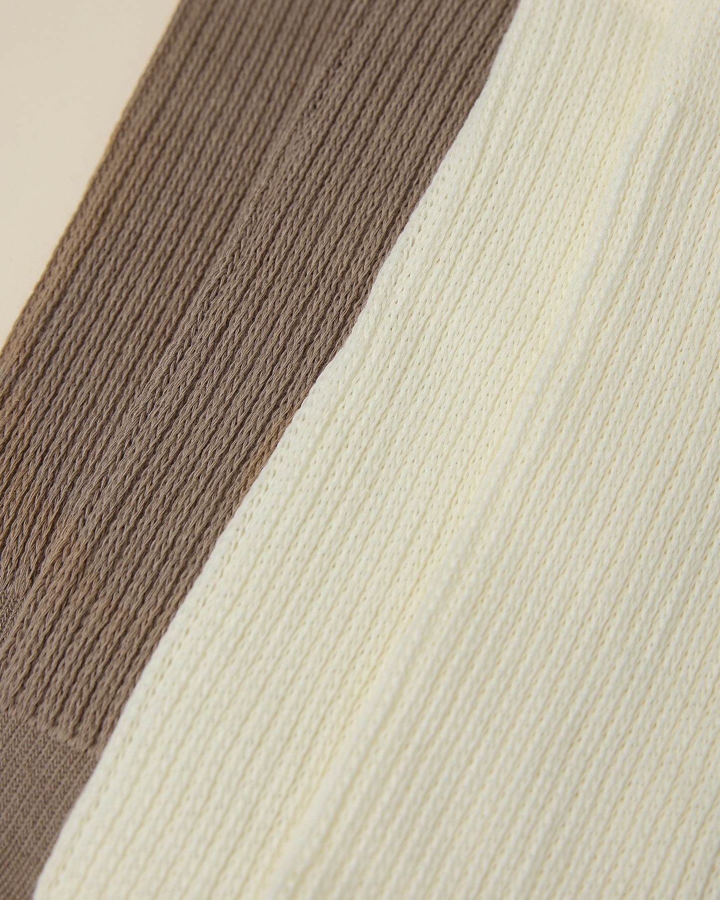 Close up on the cozy cuffs of two pair of Non-Slip Slouchy Socks in Cream and Taupe on a beige background