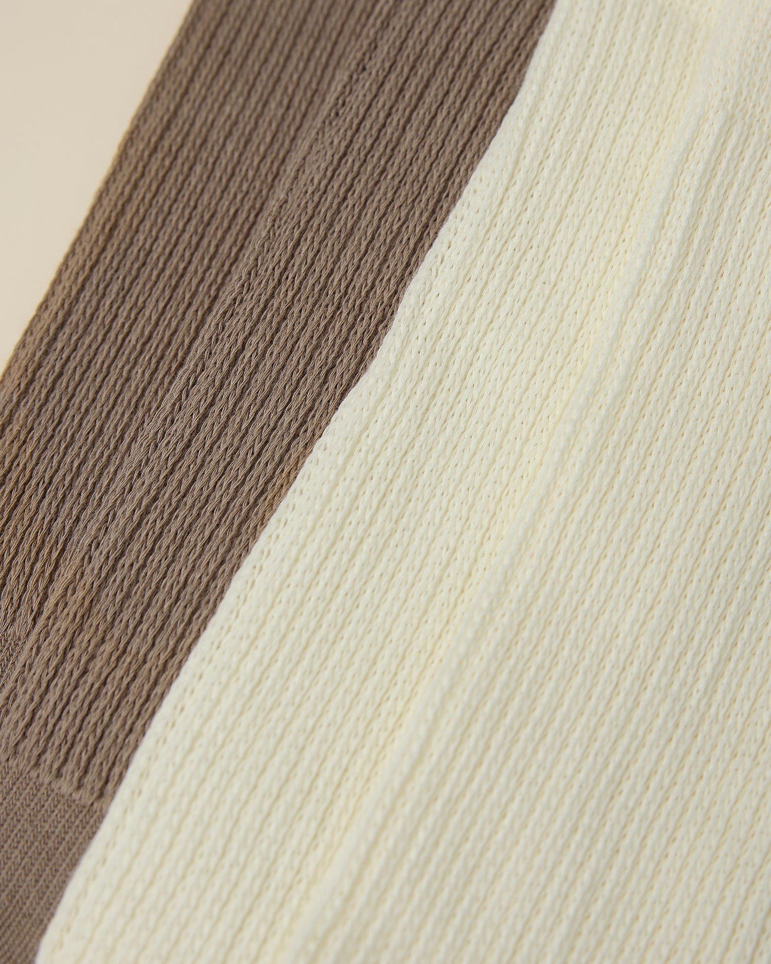 Close up on the cozy cuffs of two pair of Non-Slip Slouchy Socks in Cream and Taupe on a beige background