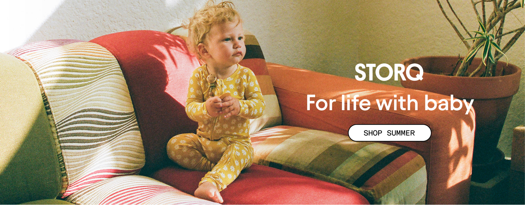 Photo of baby in Bamboo Baby Pajama in Yellow Daisies on a patterned couch. White text: STORQ, For life with baby. White button: Shop Summer.