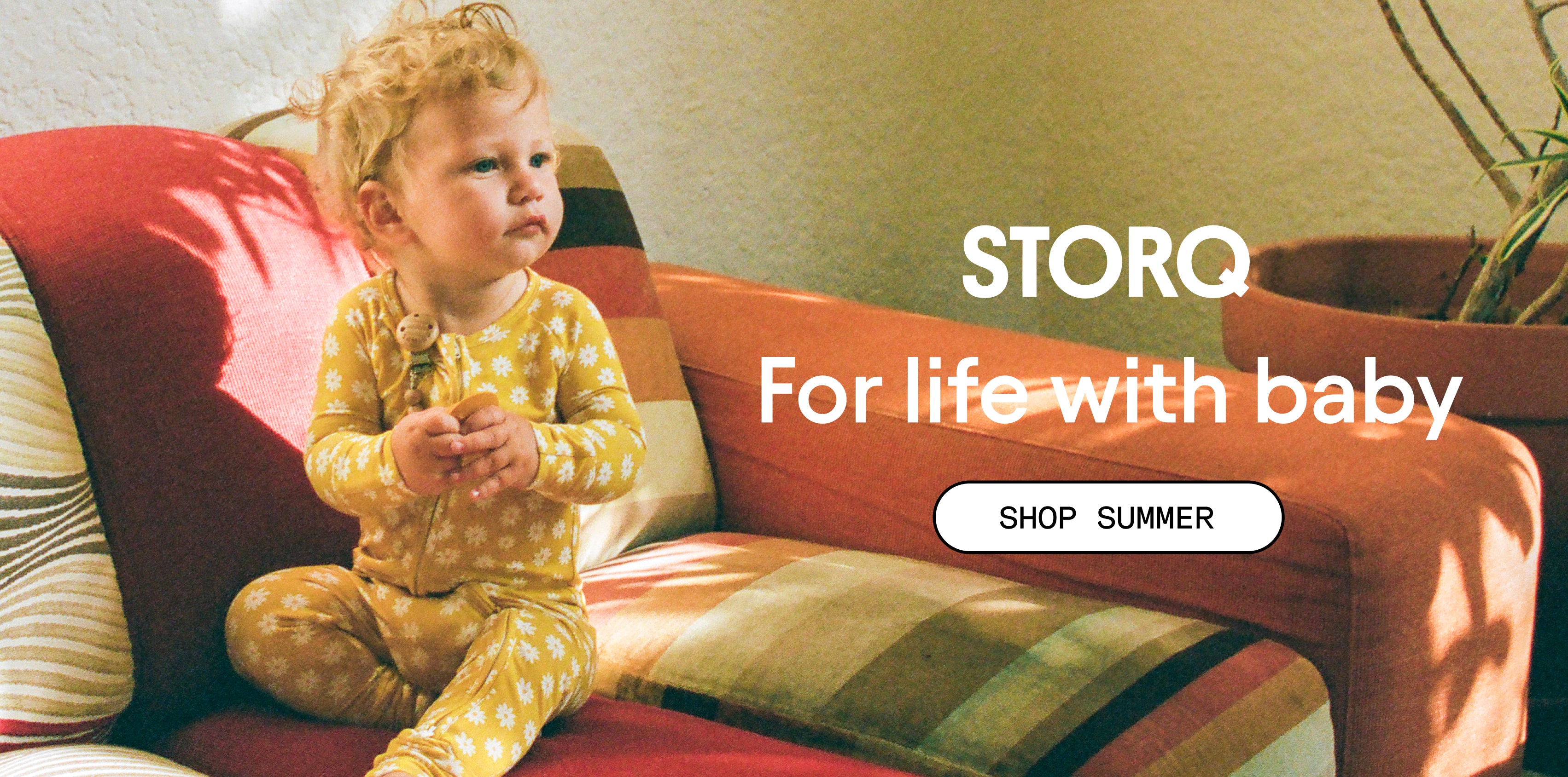 Photo of baby in Bamboo Baby Pajama in Yellow Daisies on a patterned couch. White text: STORQ, For life with baby. White button: Shop Summer.