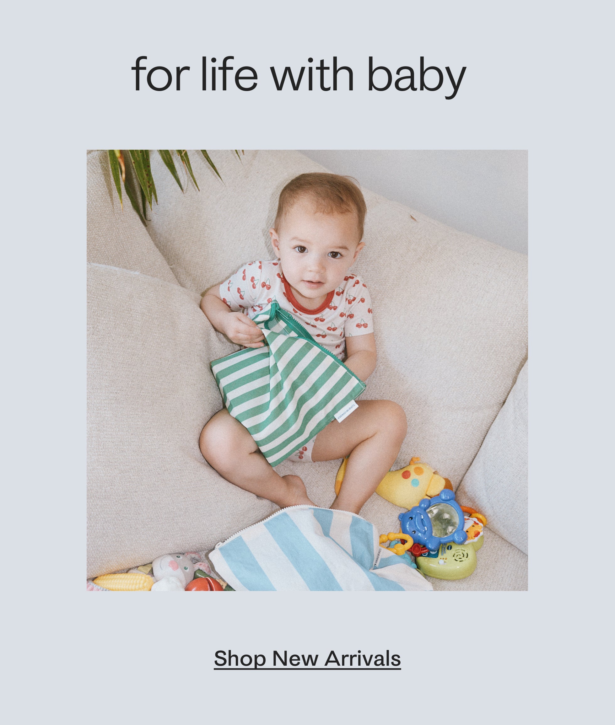 Black text on a grey background, stating: for life with baby, shop new arrivals. Photo of a toddler wearing Bamboo Short Sleeve & Shorts Set in Ivory Cherries, sitting on couch with many toys, while reaching into Zipper Pouch Three-Piece Set in Stripe. 