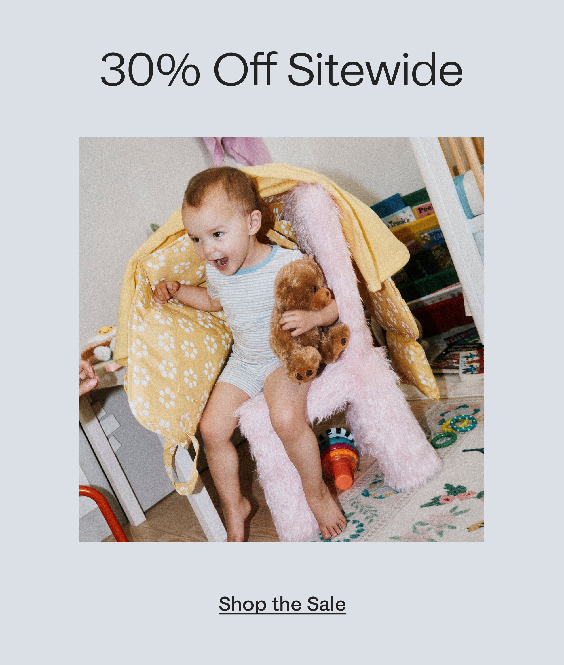 Black text on white background: 30% Off Sitewide. Image of toddler playing on pink fuzzy chair, holding teddy bear, under blankets. Black link text: Shop the Sale