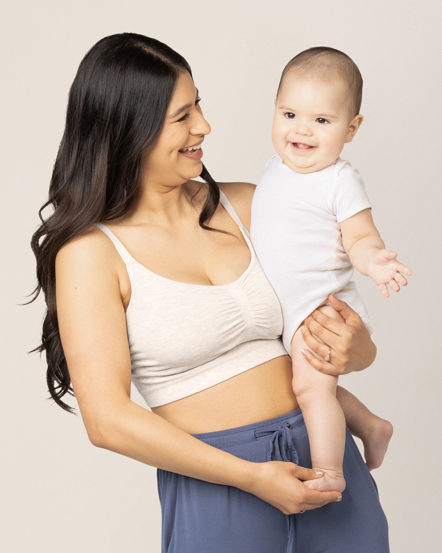 Model holding her baby while wearing the Sublime® Bamboo Hands-Free Pumping Lounge & Sleep Bra in Oatmeal Heather @model_info:Nohely is wearing a Medium.