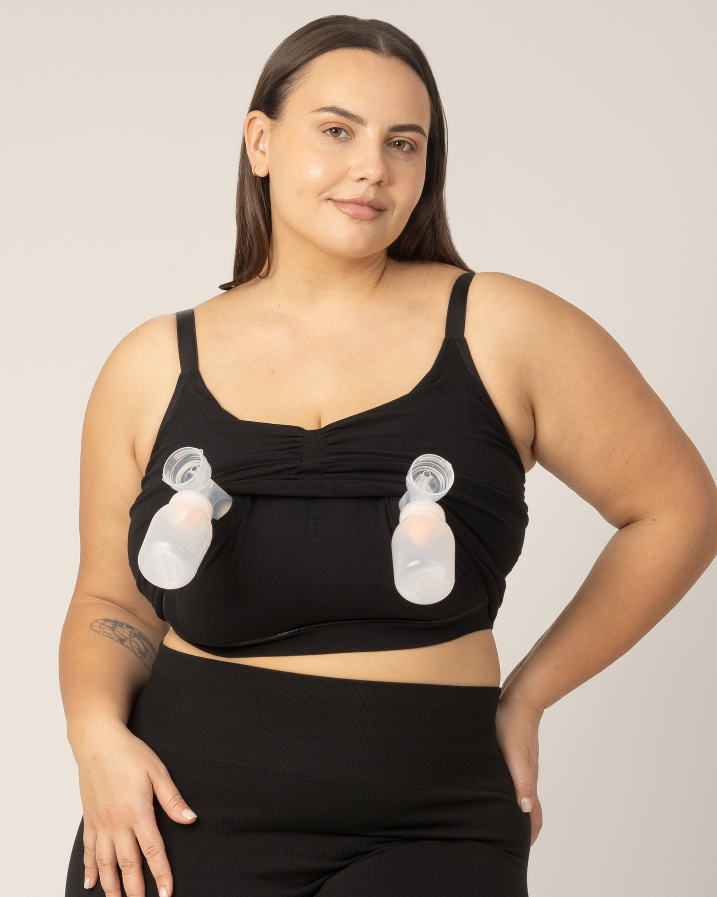 Super busty model wearing the Sublime Hands-Free Pumping & Nursing Sleep and Lounge Bra in Black. She pulled up the pumping layer to insert pumps for hands-free pumping access. @model_info:Anna is wearing a Large Super Busty.