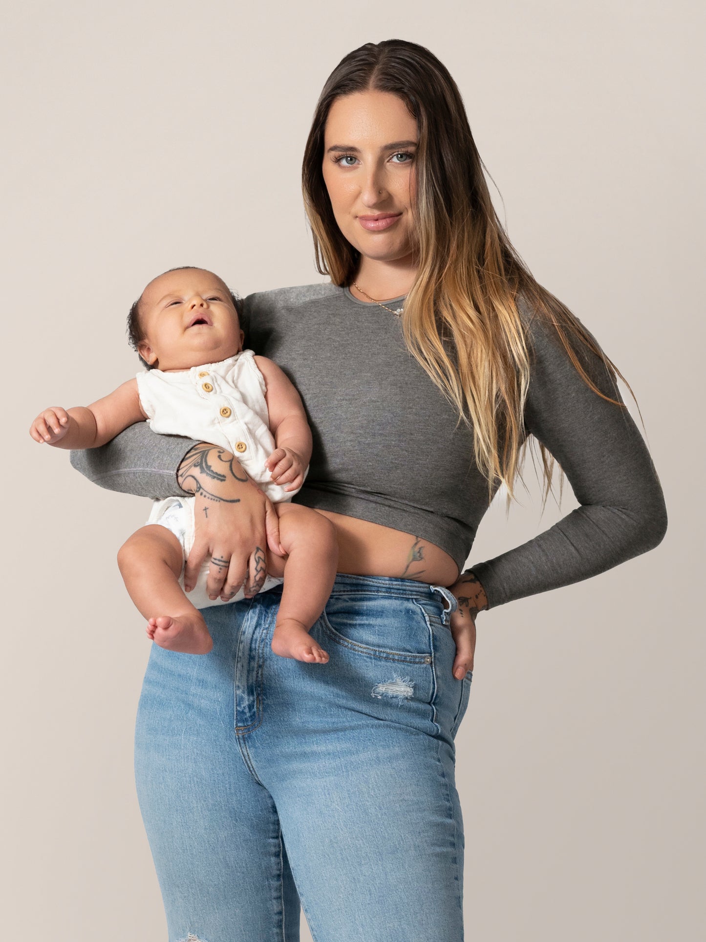 Front view of model wearing the Sublime® Bamboo Maternity & Nursing Cropped Long Sleeve Top in Charcoal, and holding baby. 