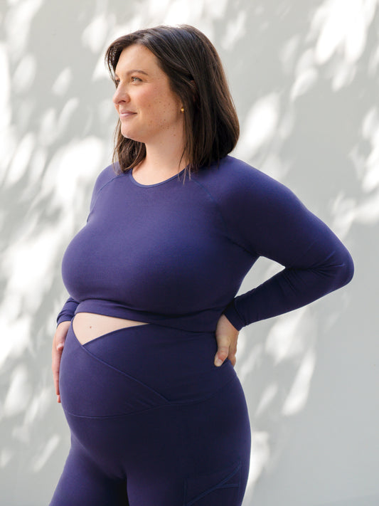 3/4 angle of model standing outside wearing the Sublime® Bamboo Maternity & Nursing Cropped Long Sleeve Top in Navy. @model_info:Shelby is wearing an X-Large.