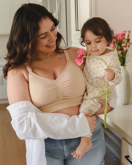 Model wearing the Sublime® Hands-Free Pumping & Nursing Bra in Beige while holding baby