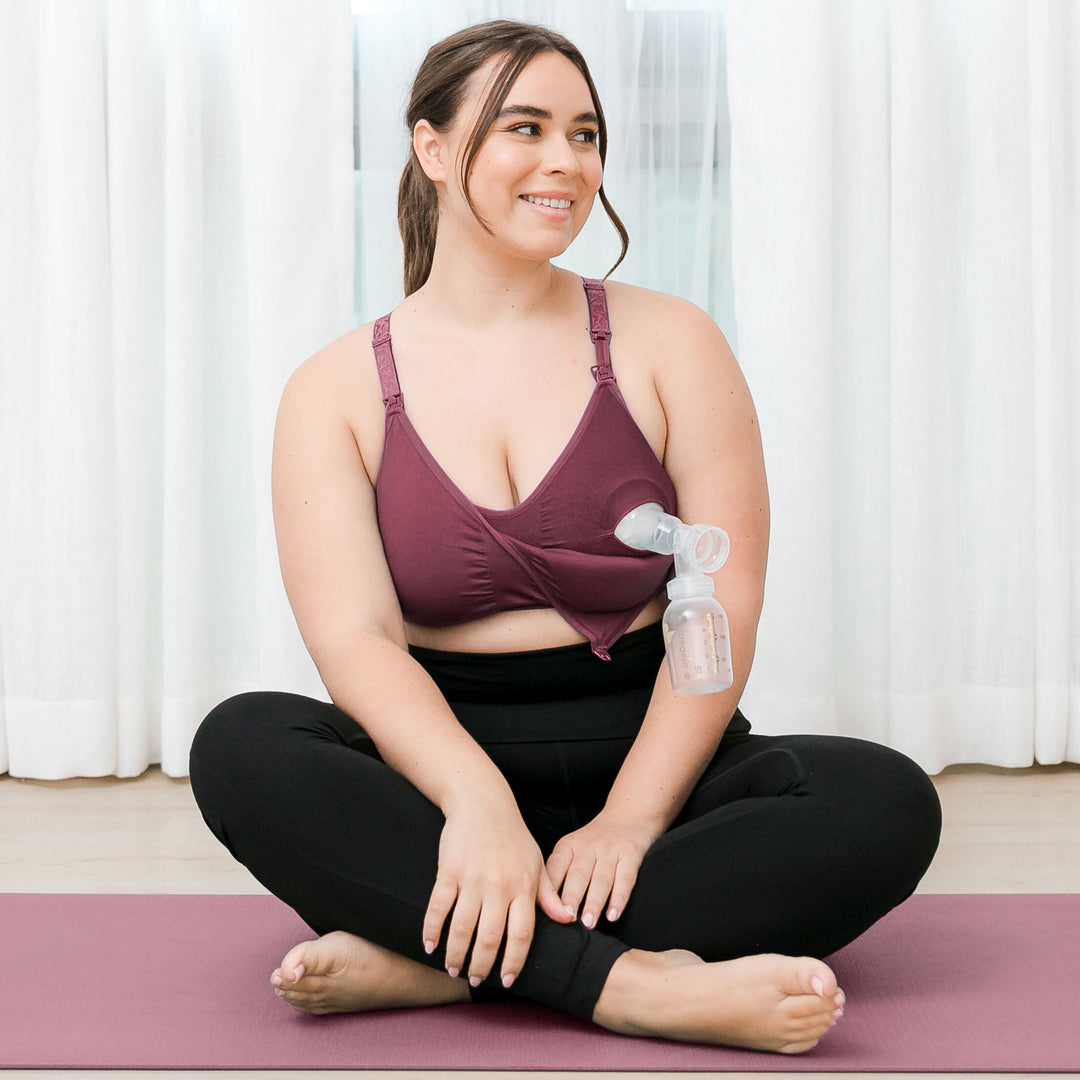 Model wearing the Sublime® Hands-Free Pumping & Nursing Sports Bra in Fig sitting on a yoga mat. @model_info:Venezia is wearing an X-Large Busty.