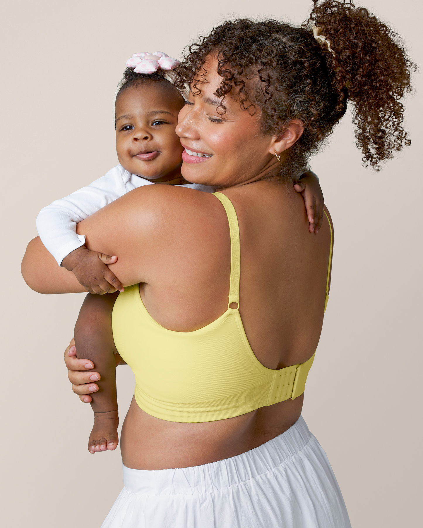 Side back view of model hugging baby and wearing the Sublime® Hands-Free Pumping & Nursing Bra Light Lemon