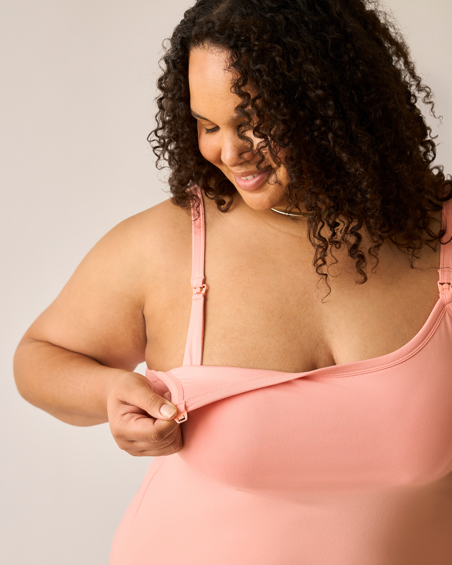 Woman wearing a pink dress. showing clip-down nursing access, against a neutral background