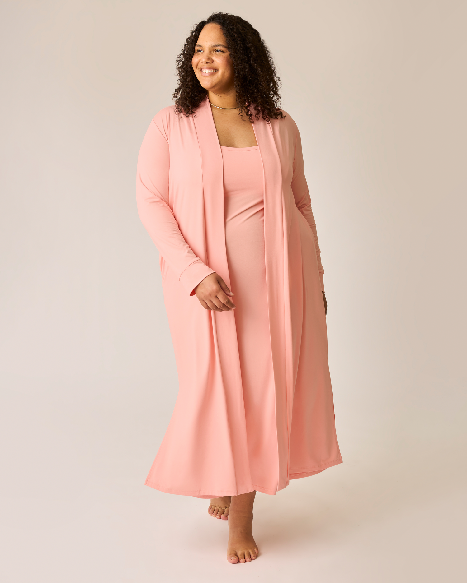 Woman wearing a pink lounge dress and matching long cardigan on a plain background@model_info:Ionna is 5'11" and wearing a 2X.