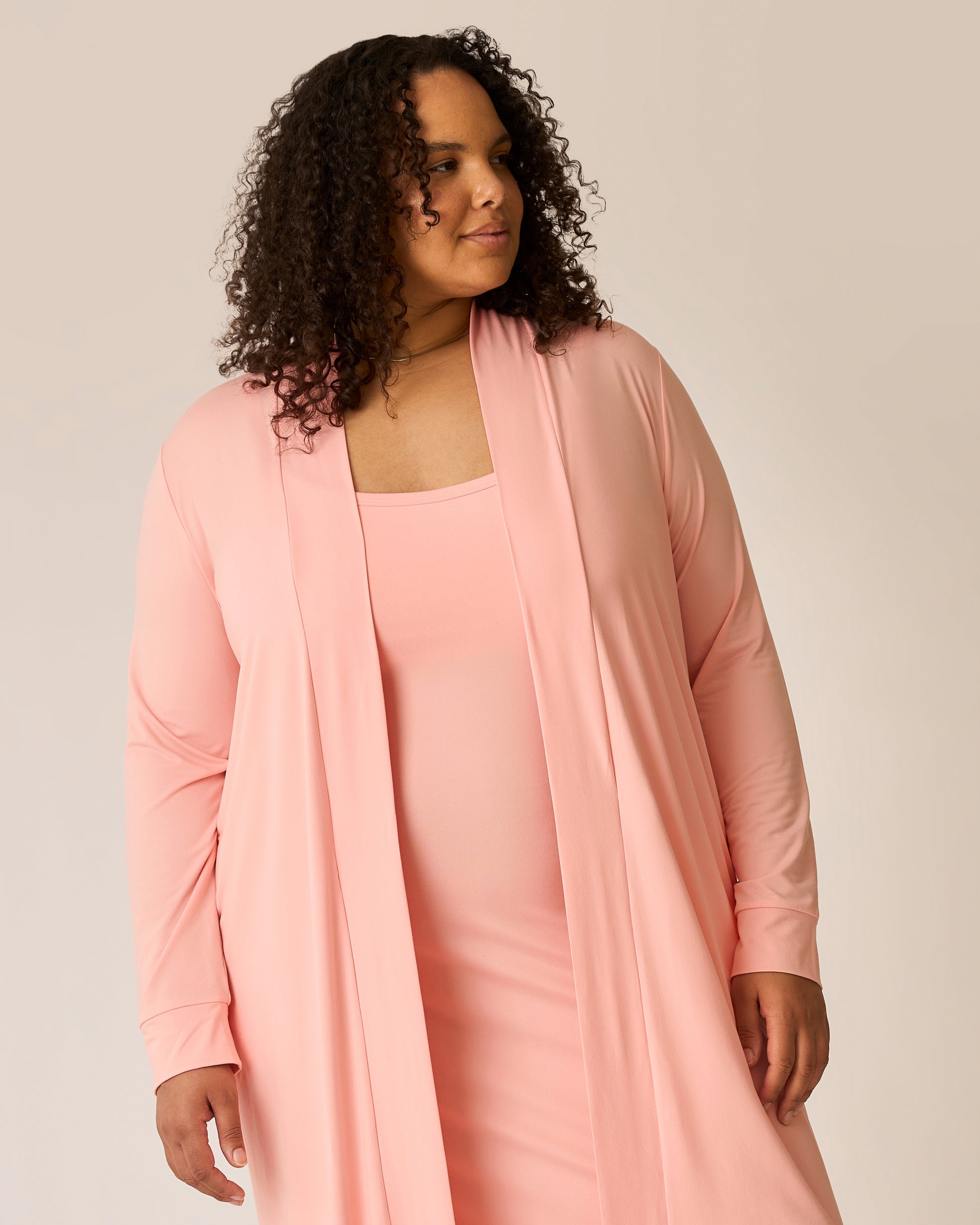 Woman wearing a pink lounge dress with a matching long cardigan against a plain background