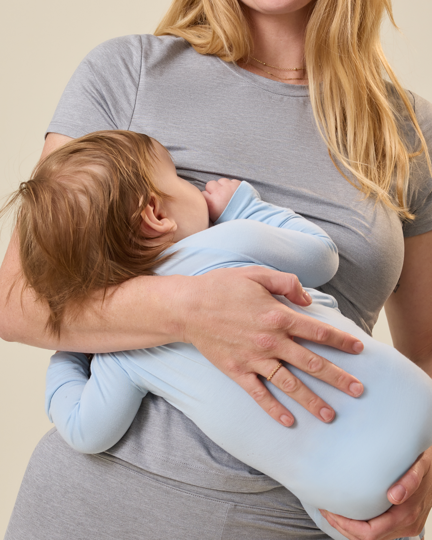 Woman wearing a grey heather lounge set, holding and nursing a baby against a neutral background@model_info:Lauren is 5'8" and wearing a Medium.