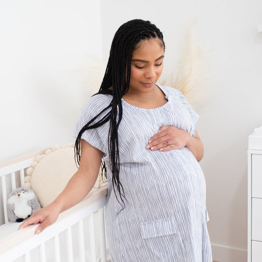 Pregnant model wearing the Universal Labor & Delivery Gown in Pinstripe looking down at her stomach. @model_info:Ruby is wearing a S/M/L.