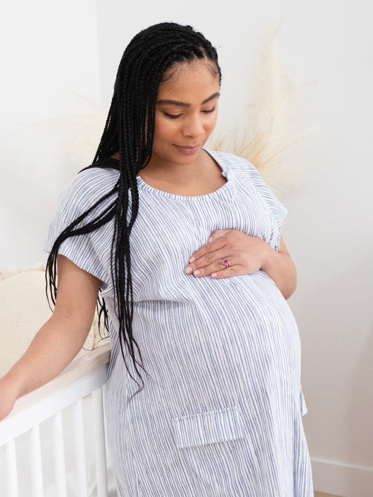 Pregnant model wearing the Universal Labor & Delivery Gown in Pinstripe looking down at her stomach. @model_info:Ruby is wearing a S/M/L.