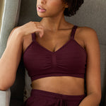 Woman wearing a maroon sports bra and shorts against a neutral background