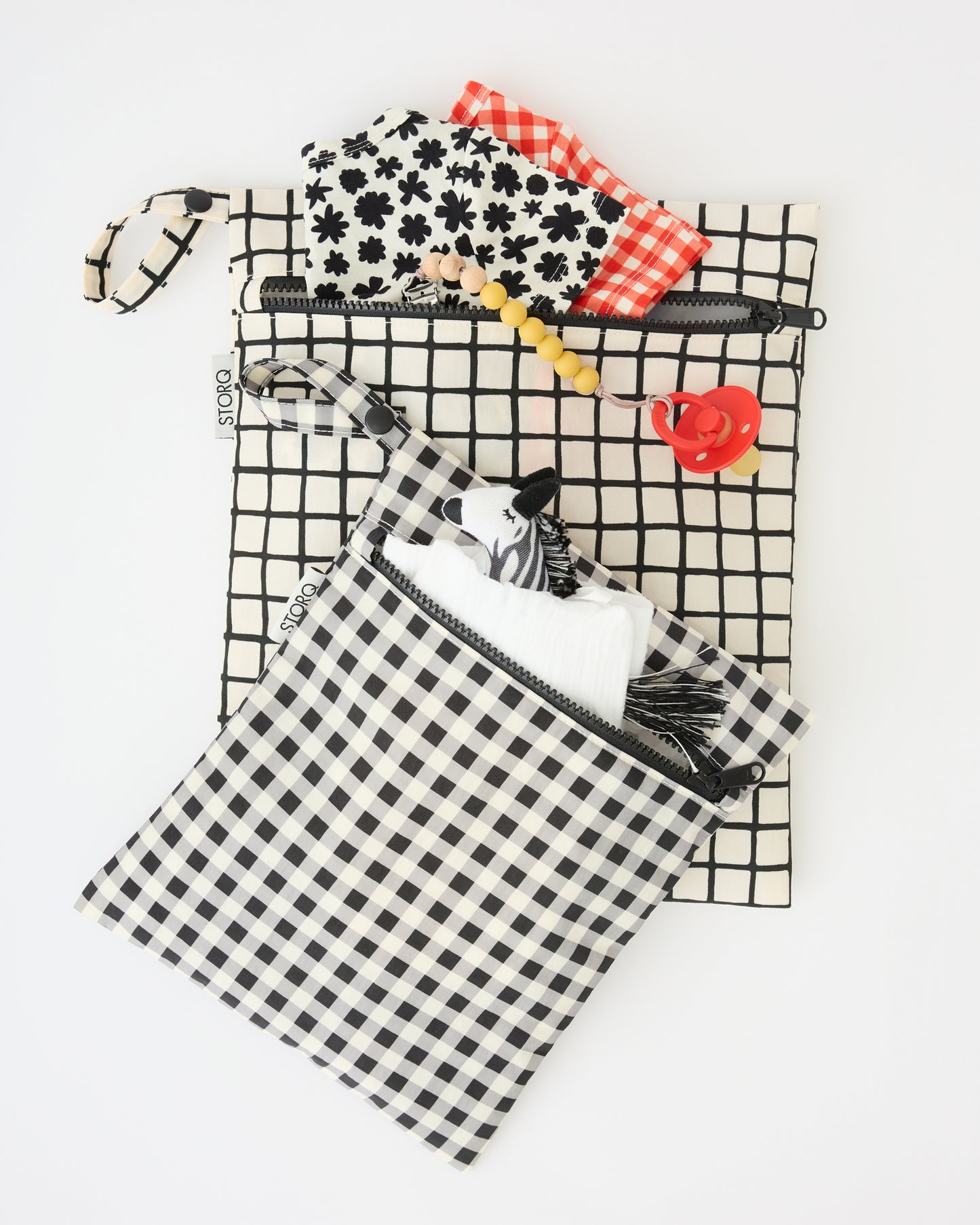 Wet/Dry Bag Set in Black Grid with diapers, zebra lovey, pacifier and onesies peeking out of the bags, on a beige background.