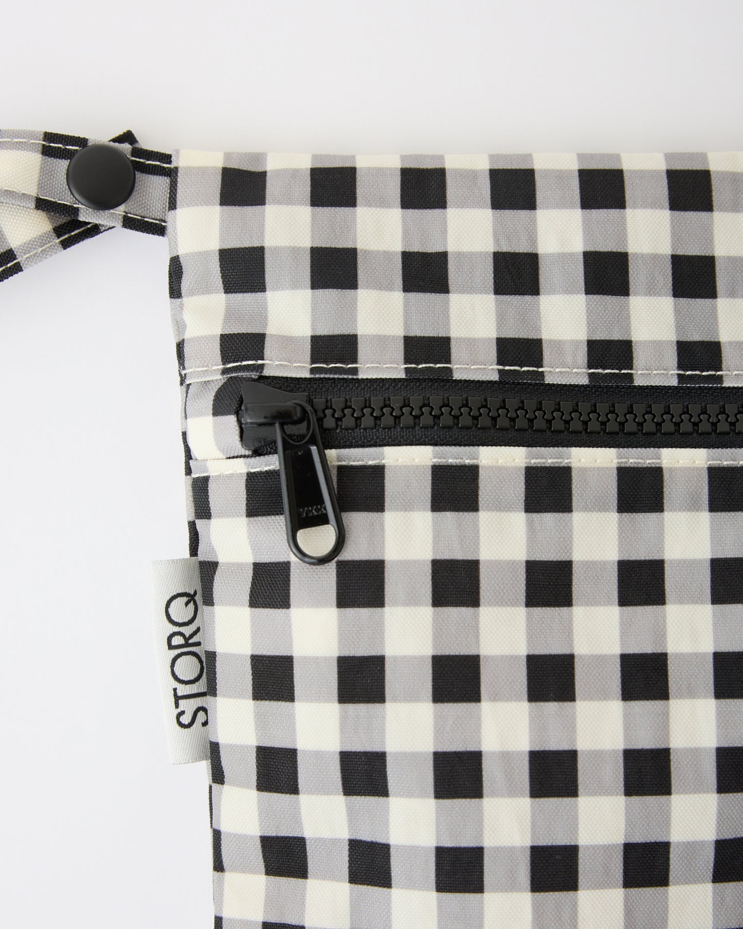 Close up of the zipper and snap loop of the Wet/Dry Bag Set in Black Grid on a beige background.