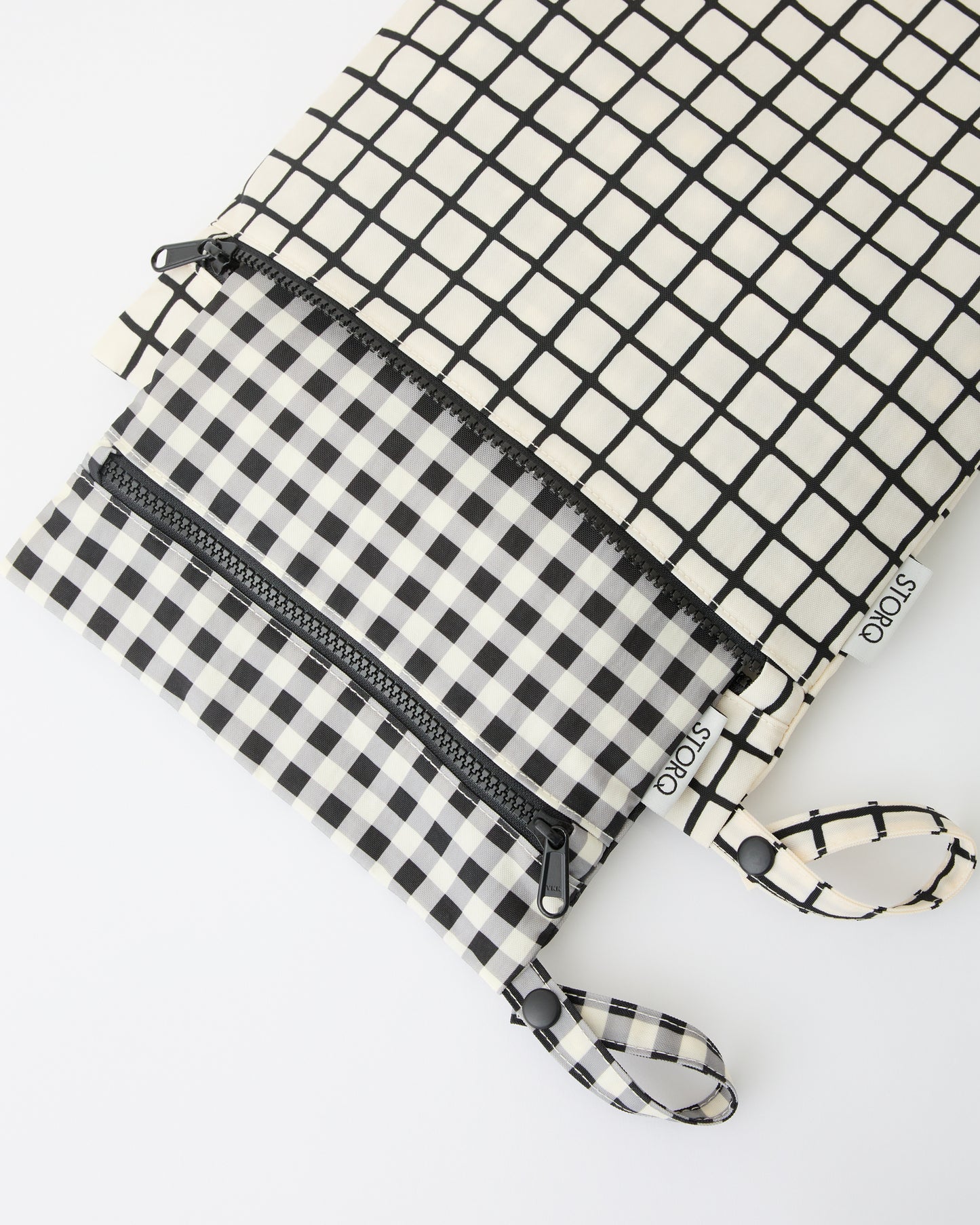 Wet/Dry Bag Set in Black Grid, the smaller bag fitting inside the larger, on a beige background.