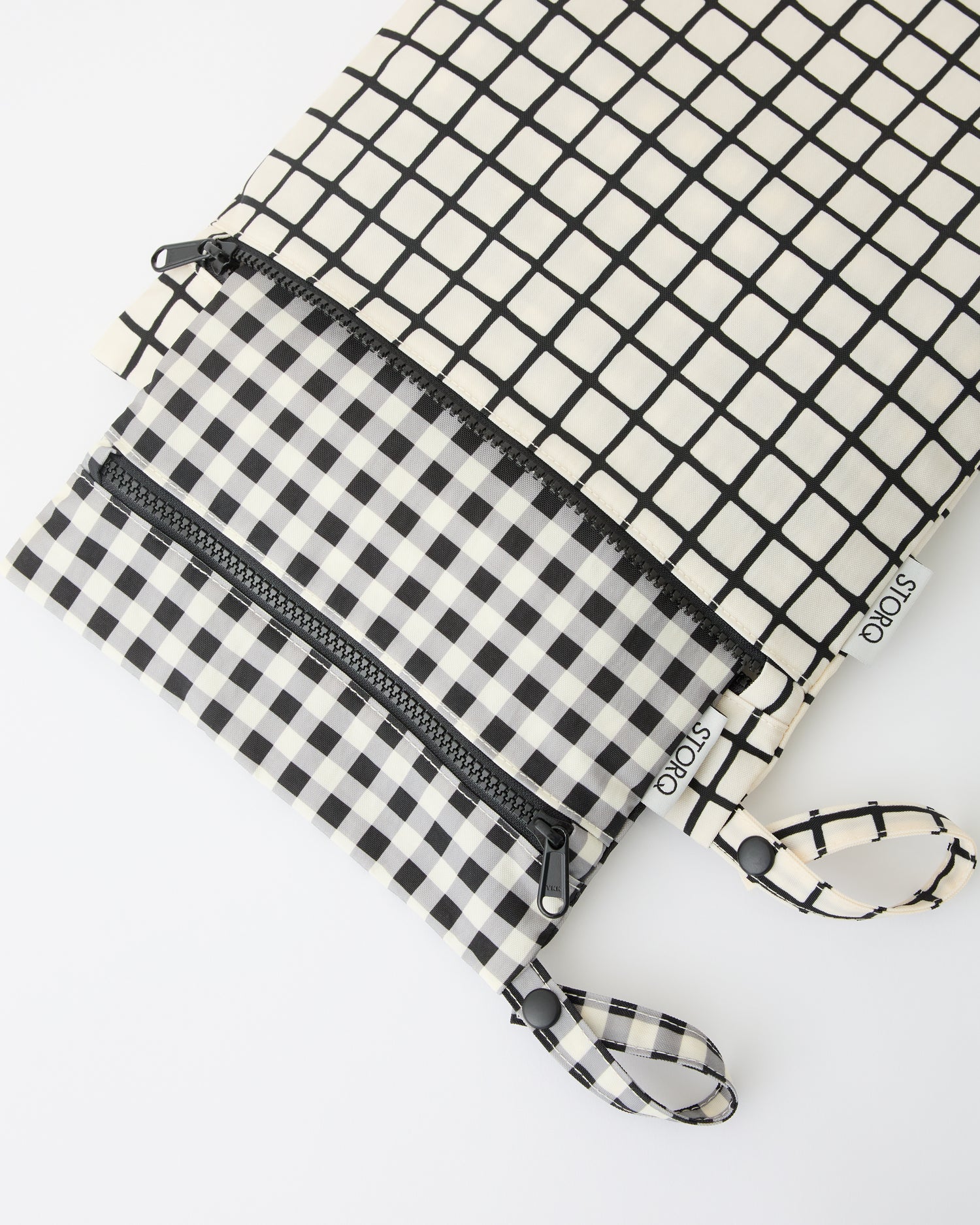 Wet/Dry Bag Set in Black Grid, the smaller bag fitting inside the larger, on a beige background.