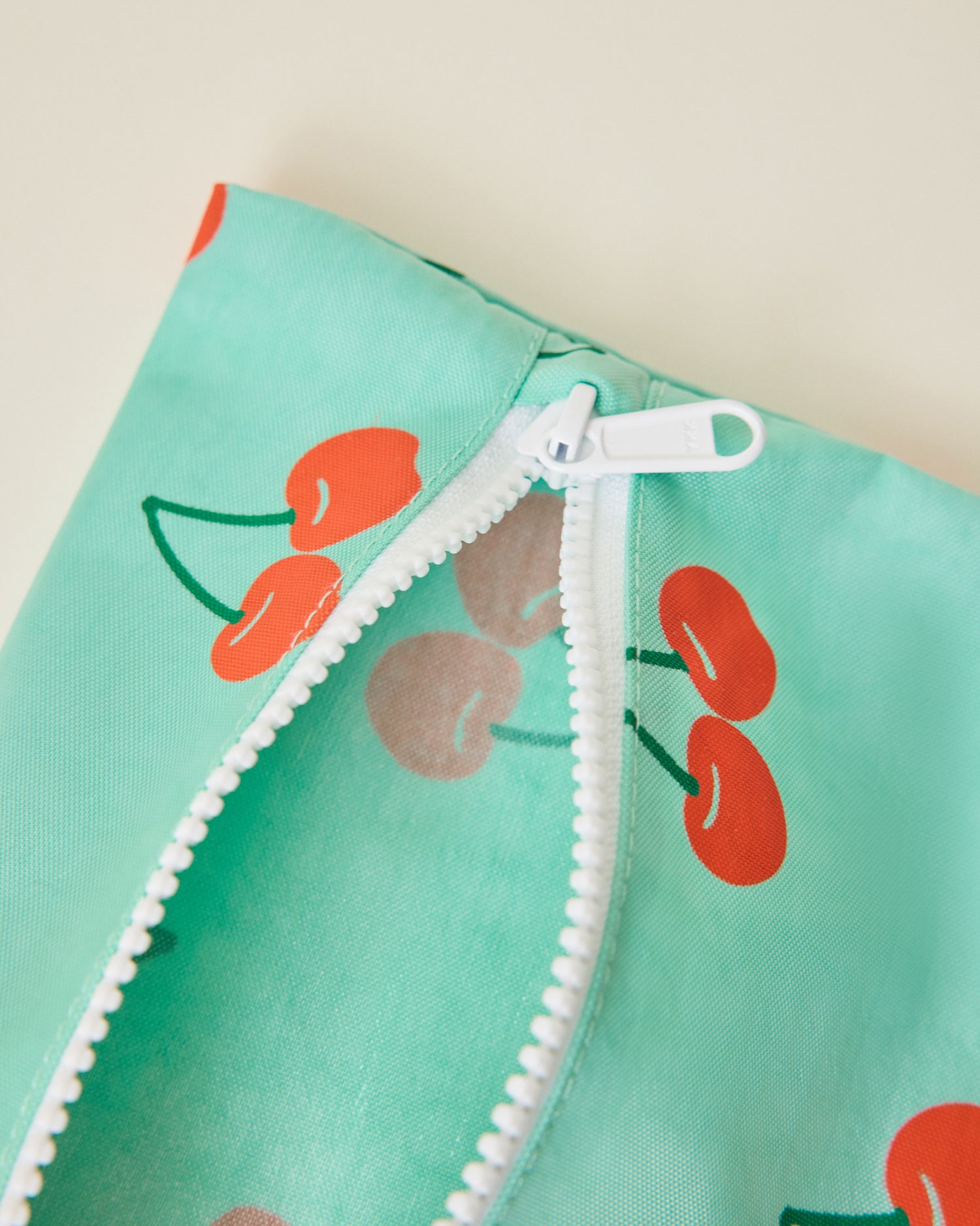 Close up of Wet/Dry Bag Set in Cherries print unzipped, on beige background