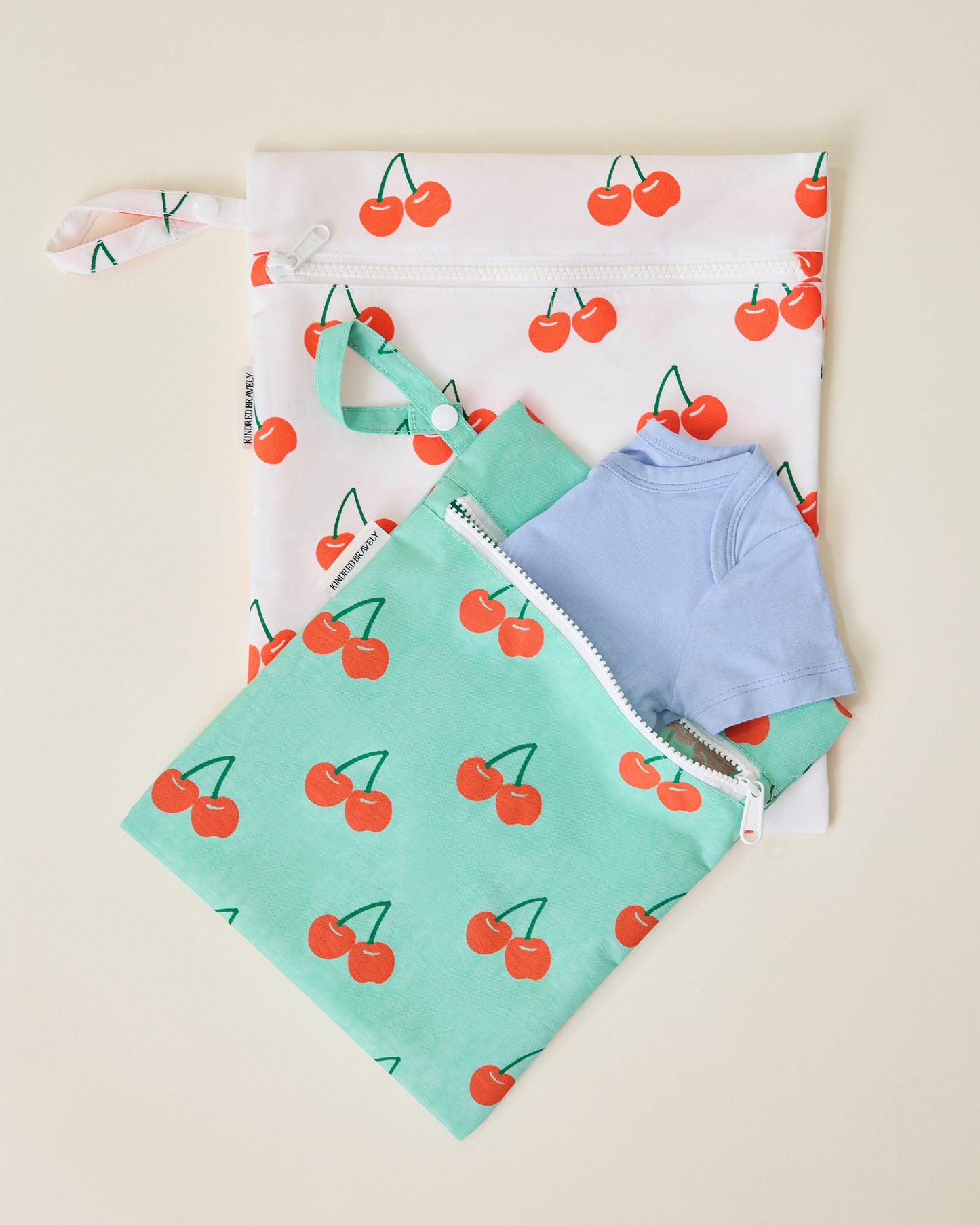 Wet/Dry Bag Set in Cherries print, dry bag is holding a onesie on beige background