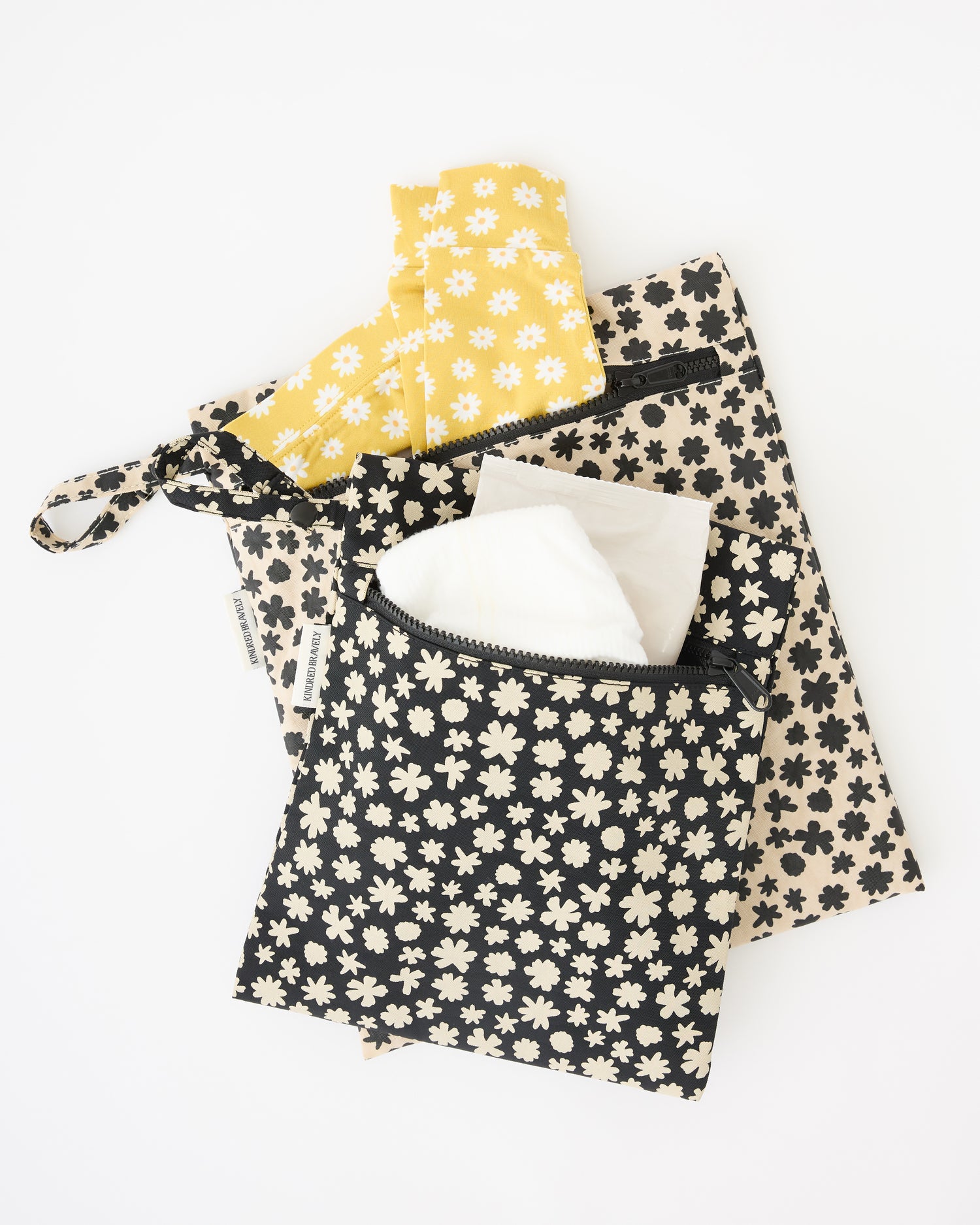 Wet/Dry Bag Set in Cream Chamomiles with diapers, wipes and Bamboo Baby Two-Piece Pajama Set in Yellow Daisies sticking out, on a beige background