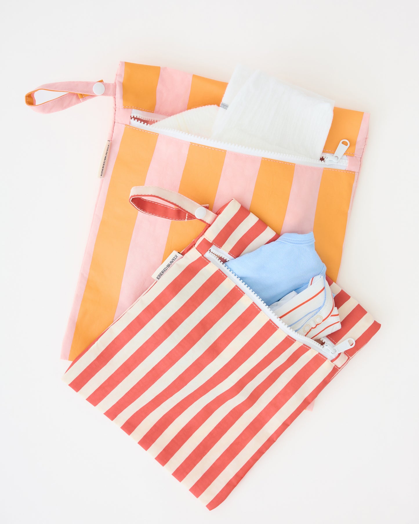 Close up of Wet/Dry Bag Set in Pink Stripe holding a diaper, wipes and onesies on a beige background