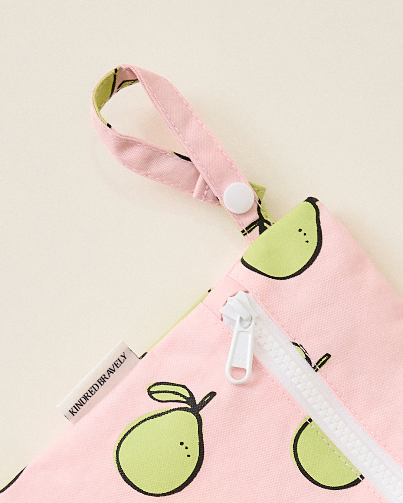 Close up of Wet/Dry Bag Set in Pomelo print, displaying strap snap button for easy organization, on beige background