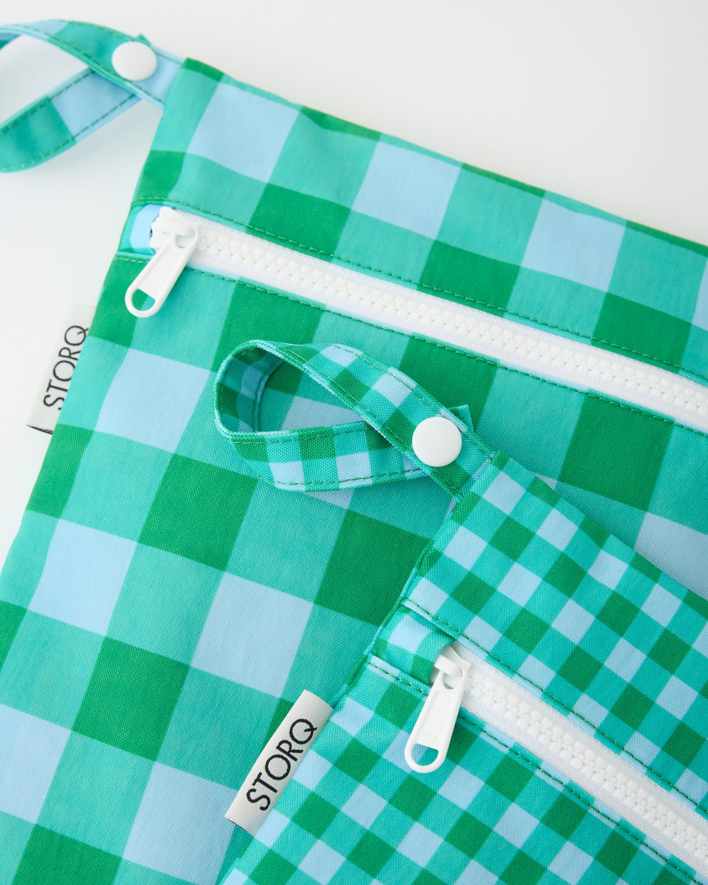 A close up of the snap loop and zipper of the Wet/Dry Bag Set in Teal Gingham on a beige background.