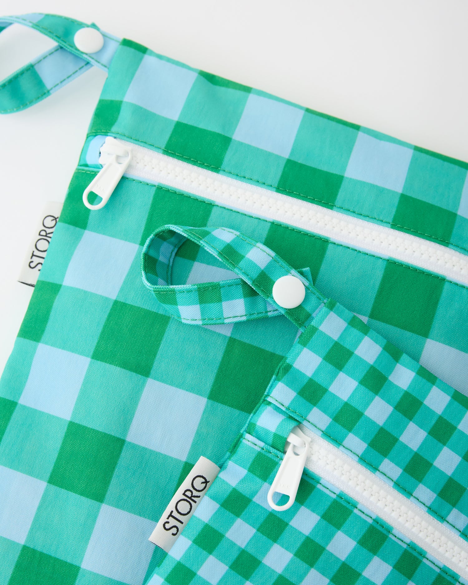 A close up of the snap loop and zipper of the Wet/Dry Bag Set in Teal Gingham on a beige background.