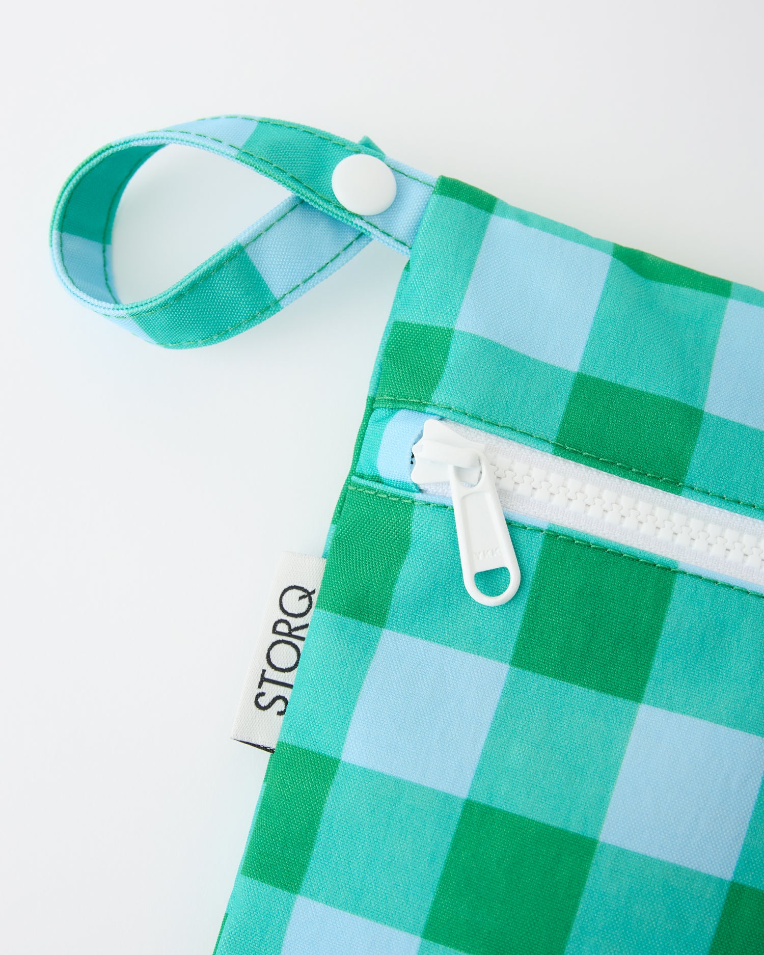 A close up of the snap loop and zipper of the Wet/Dry Bag Set in Teal Gingham on a beige background.