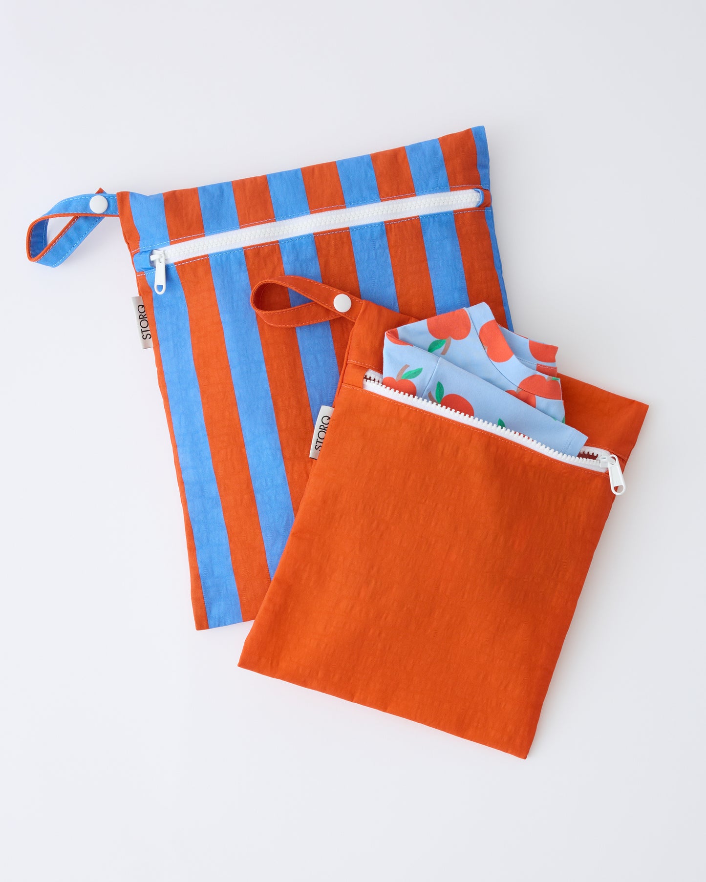 Wet/Dry Bag Set in Blue & Rust Stripe on a beige background with a Blue Apple shirt sticking out of the smaller bag. 