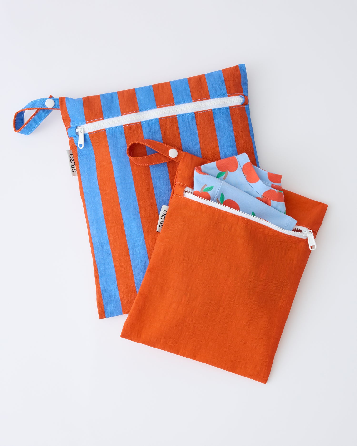 Wet/Dry Bag Set in Blue & Rust Stripe on a beige background with a Blue Apple shirt sticking out of the smaller bag. 