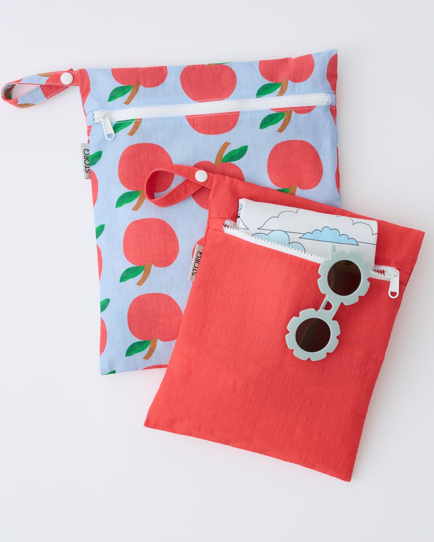 Wet/Dry Bag Set in Blue Apple with shirt and sunglasses sticking out of smaller bag, on a beige background.