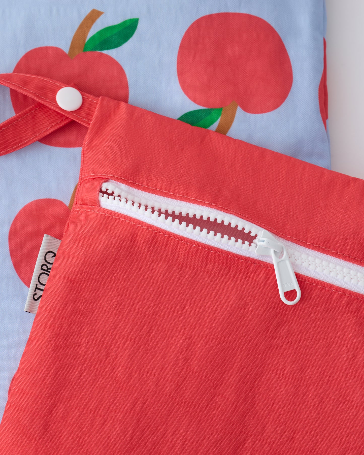 Close up of the zippers and snap loop of the Wet/Dry Bag Set in Blue Apple on a beige background.