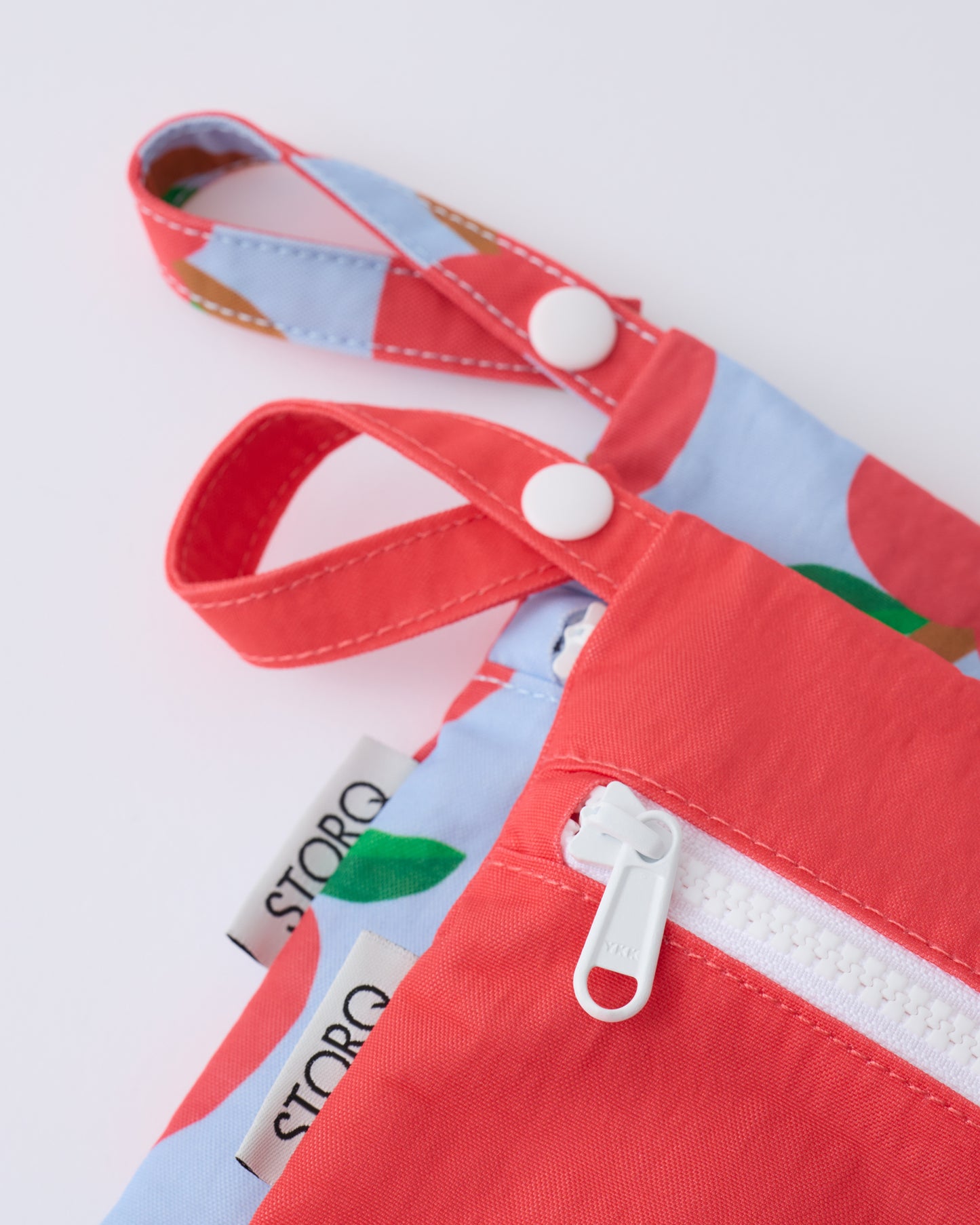 Close up of the zippers and snap loop of the Wet/Dry Bag Set in Blue Apple on a beige background.
