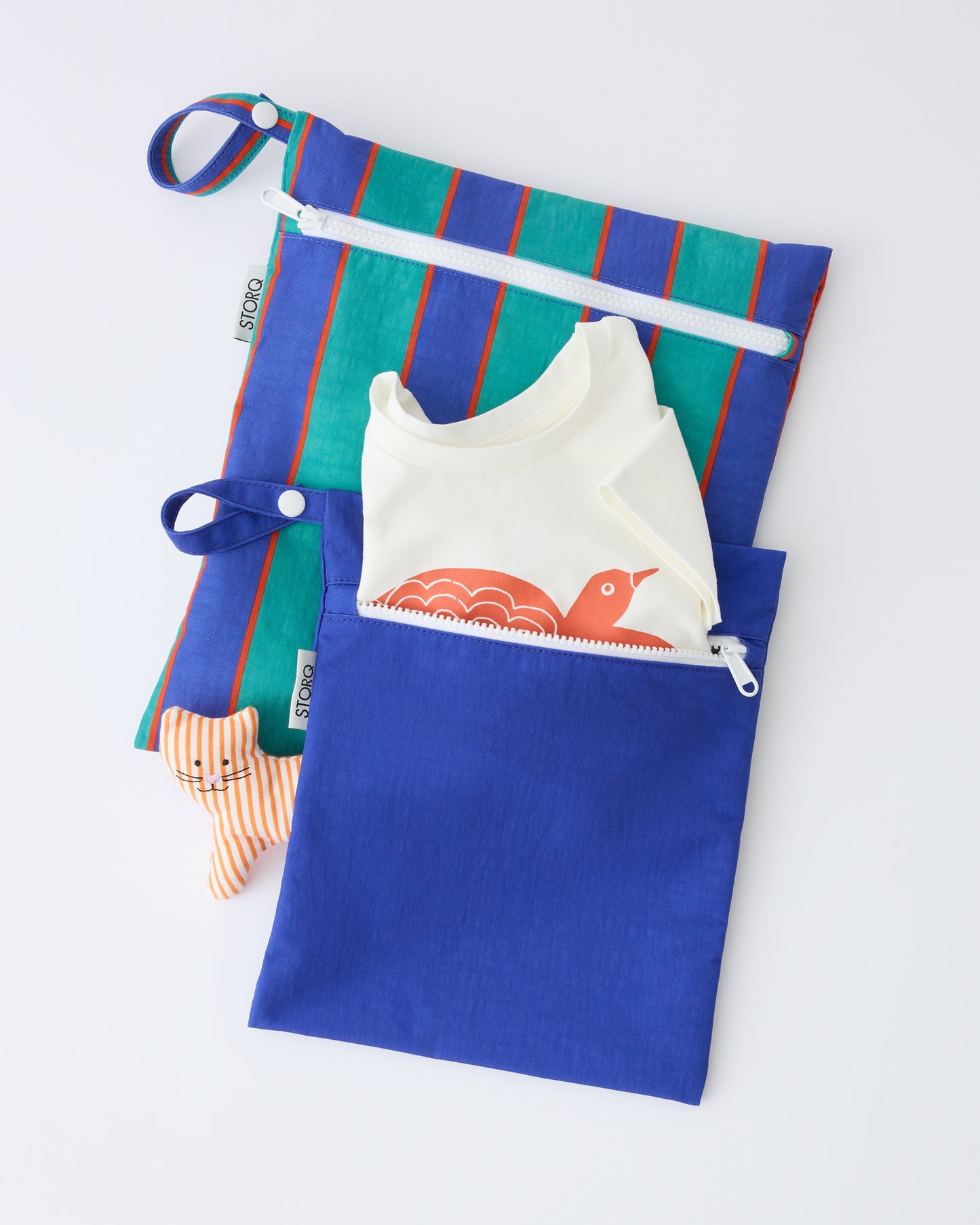 Wet/Dry Bag Set in Navy & Green Stripe with a shirt sticking out of the smaller bag, and a toy underneath, on a beige background.