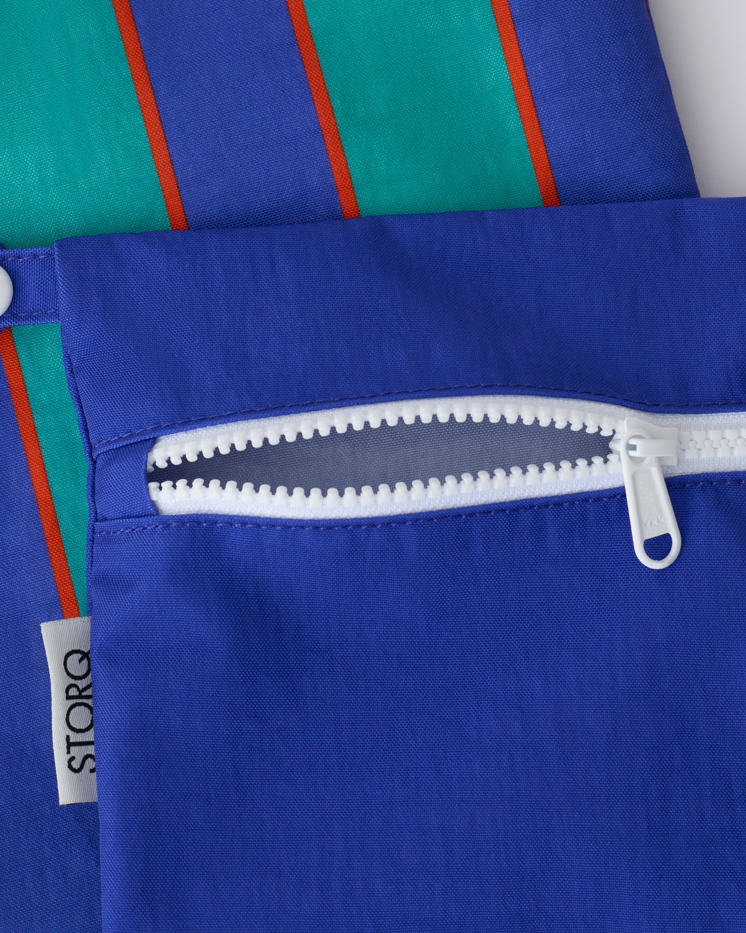 Close up of the zippers and snap loop of the Wet/Dry Bag Set in Navy & Green Stripe on a beige background.