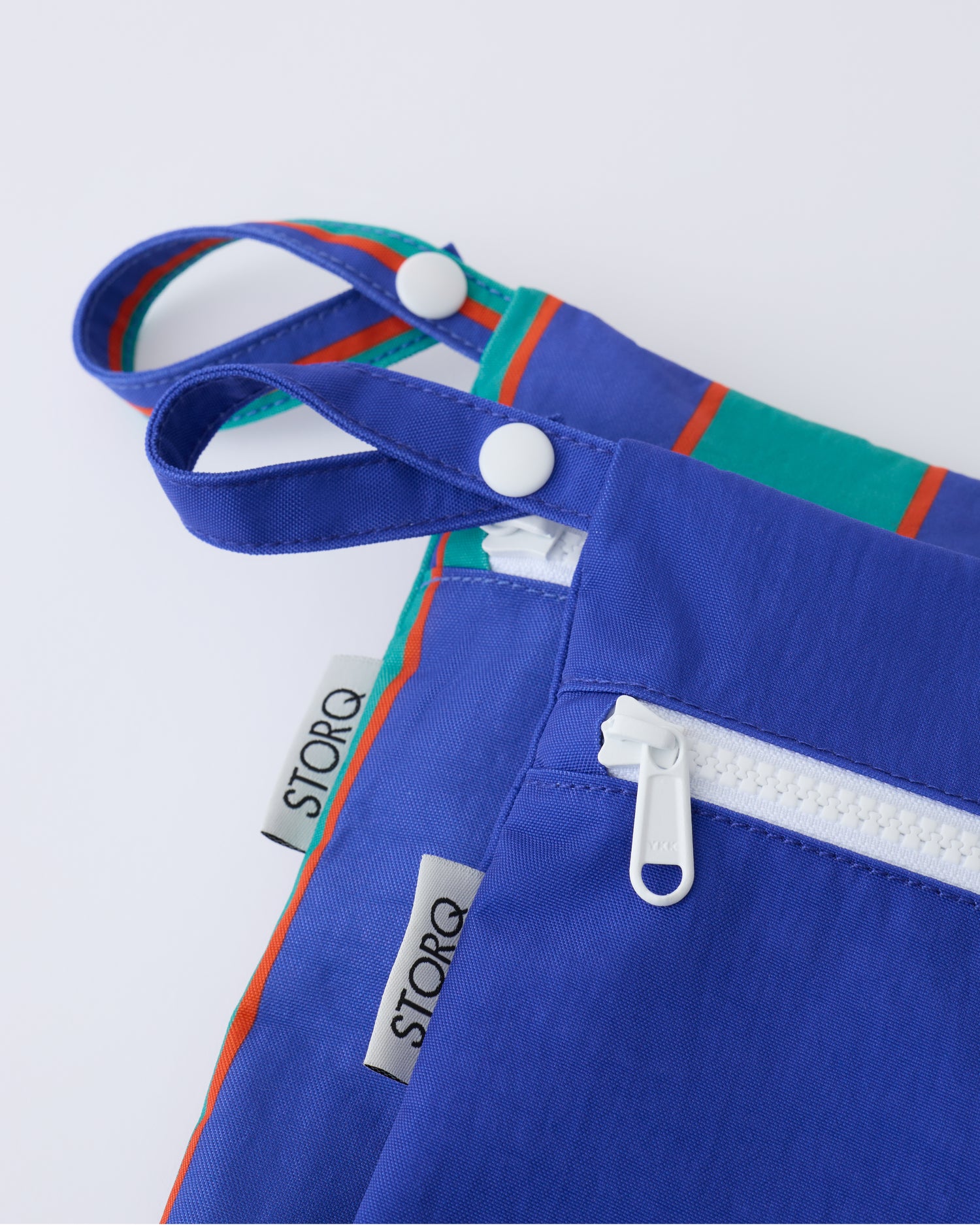 Close up of the zippers and snap loop of the Wet/Dry Bag Set in Navy & Green Stripe on a beige background.